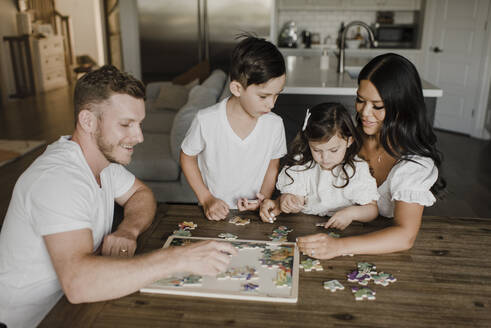 Smiling parents solving puzzle with kids over table at home - SMSF00208