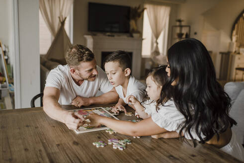Smiling parents solving jigsaw puzzle with kids over table at home - SMSF00209
