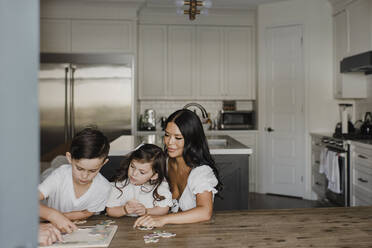 Lächelnde Eltern, die mit ihren Kindern am Tisch zu Hause ein Rätsel lösen - SMSF00210