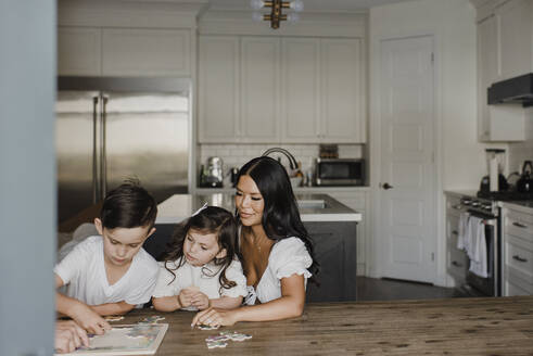 Smiling parents solving puzzle with children over table at home - SMSF00210