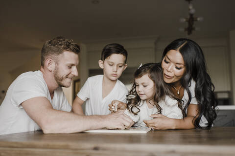 Smiling parents solving jigsaw puzzle with kids on table at home stock photo