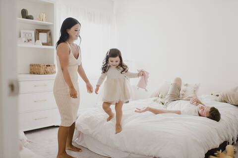 Smiling parents looking at daughter standing on bed at home stock photo