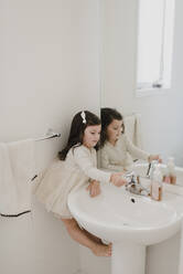 Mädchen wäscht die Hand und balanciert zwischen Wand und Waschbecken im Badezimmer - SMSF00222