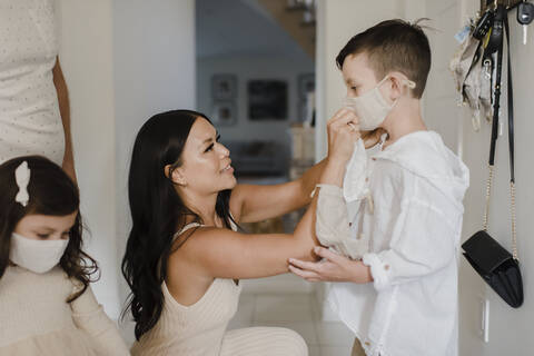 Mother covering son's face with protective mask at home during COVID-19 stock photo