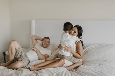 Son embracing mother while father lying on bed in bedroom - SMSF00231