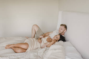 Lächelnde Frau liegt mit männlichem Partner im Schlafzimmer - SMSF00233