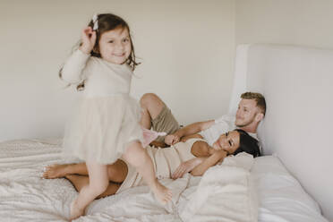 Verspielte Tochter springt auf dem Bett, während die Eltern im Schlafzimmer liegen - SMSF00234