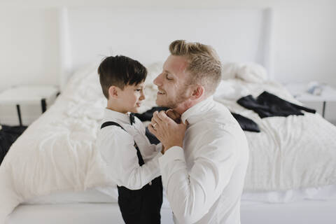 Lächelnder Vater und Sohn, die sich im Schlafzimmer für die Hochzeit anziehen, lizenzfreies Stockfoto