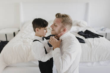 Lächelnder Vater und Sohn, die sich im Schlafzimmer für die Hochzeit anziehen - SMSF00242