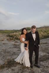 Smiling bridegroom holding hands while walking in field - SMSF00248