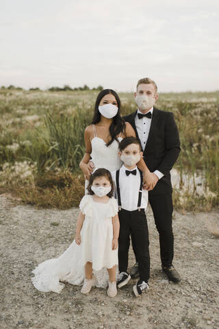 Parents and children in wedding dress wearing protective face mask while standing in field during COVID-19  stock photo