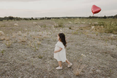 Cute girl with heart shape balloon walking in field stock photo