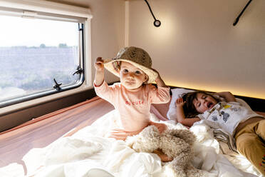 Niedliches kleines Mädchen mit Hut, das neben seiner Schwester sitzt und im Wohnmobil aufwacht - GEMF04101