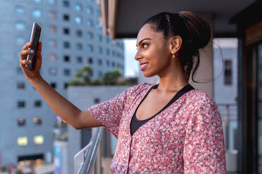 Beautiful smiling woman taking selfie in balcony - EGAF00677