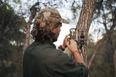 Älterer männlicher Fotograf, der eine Kamera auf einem Baumstamm im Wald positioniert - SASF00006