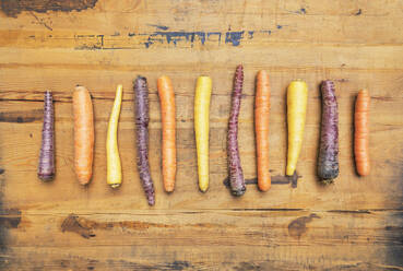 Row of purple, orange and yellow carrots on wooden surface - GWF06738