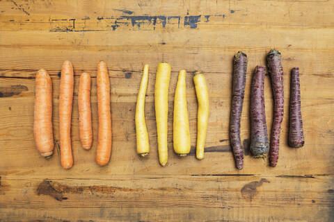 Row of purple, orange and yellow carrots on wooden surface stock photo