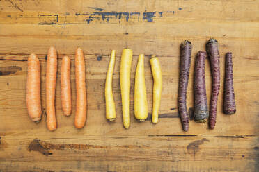 Row of purple, orange and yellow carrots on wooden surface - GWF06739