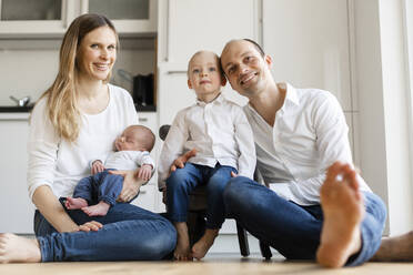 Smiling parents holding baby boys while sitting on floor at home - SAJF00095