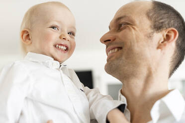 Father smiling while looking at baby boy while standing at home - SAJF00102