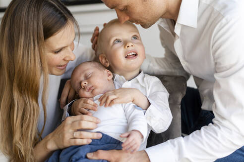 Mutter und Vater, die sich um einen kleinen Jungen kümmern, der zu Hause auf einem Stuhl sitzt - SAJF00104