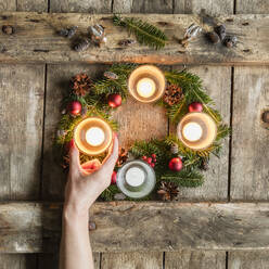 Die Hand einer Frau berührt die Glasabdeckung einer brennenden Kerze auf einem Adventskranz - EVGF03703