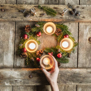 Die Hand einer Frau berührt die Glasabdeckung einer brennenden Kerze auf einem Adventskranz - EVGF03704