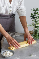 Anonyme Bäckerin in Schürze bei der Herstellung von Brötchen aus weichem Teig auf einem Tisch in der Nähe von Mehl und einem Blumenstrauß - ADSF13016