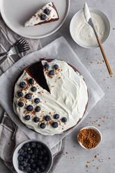 Von oben Blick auf Teller mit leckeren ganzen hausgemachten Schokoladenkuchen mit weißer Sahne in der Nähe von kleinen Stück Kuchen und Blaubeeren auf dem Tisch in der Küche platziert dekoriert - ADSF13038