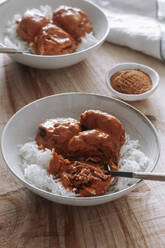 From above bowls of rice and delicious lentil meatballs with curry sauce placed near spice and napkin on wooden table at home - ADSF13044