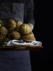 Erntehelfer in Schürze mit braunem Tablett voller frisch gebackener Muffins - ADSF13064