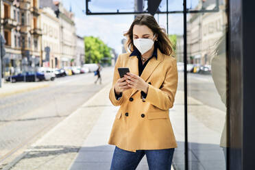 Woman in protective face mask using smart phone while waiting at tram station - BSZF01615