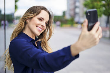 Lächelnde schöne Frau nimmt Selfie in der Stadt - BSZF01621