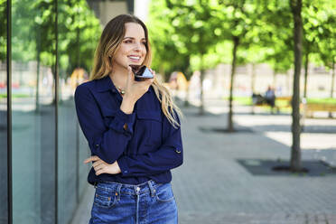 Lächelnde Frau, die den Blick abwendet, während sie über ihr Smartphone spricht - BSZF01626