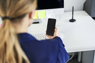 Businesswoman using smart phone at desk in creative office - BSZF01631