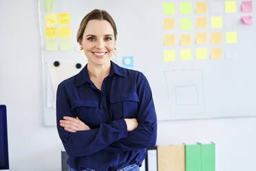 Confident businesswoman standing with arms crossed in creative office - BSZF01646