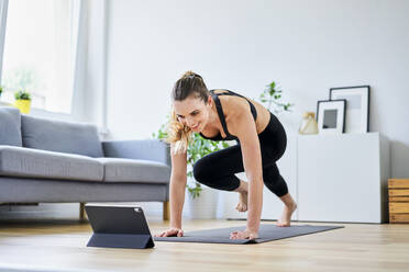 Smiling woman learning exercise on internet through digital tablet at home - BSZF01654