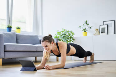 Smiling woman learning plank exercise on internet at home - BSZF01659
