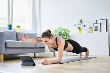 Woman extending arm during plank pose while learning exercise on internet through tablet PC - BSZF01660