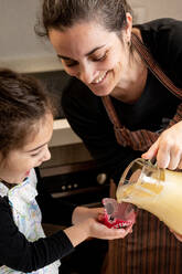 Glückliche Frau, die lächelt und Teig in einen Papierbecher gießt, während sie mit ihrer kleinen Tochter an einem Wochenendtag zu Hause Muffins zubereitet - ADSF13067