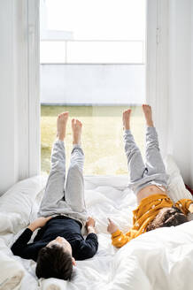 Serene Kinder in lässigen Stil entspannt auf gemütliche weiße Decke, während lehnt sich an das Fenster mit den Beinen nach oben und genießen Wochenende zusammen - ADSF13085