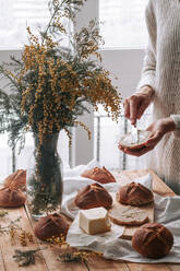 Von oben der Ernte Frau verbreiten butted auf hausgemachte Brot mit Messer auf dem Tisch mit Vase von gelben Feldblumen - ADSF13091