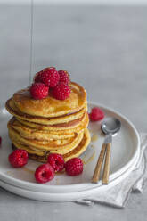 Stack of tasty pancakes with ripe raspberries placed on plate near spoons on gray background - ADSF13098