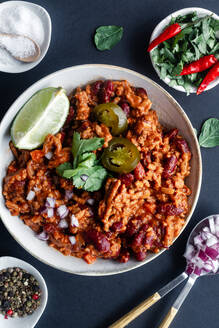 Draufsicht auf ein traditionelles würziges Chili mit Fleisch und Bohnen, garniert mit Limette und Petersilie, mit marinierter grüner Paprika, serviert in einer weißen Schale auf einem Tisch mit Zutaten - ADSF13120