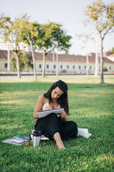 Junge Frau malt mit Aquarellfarbe in einem Buch, während sie in einem öffentlichen Park sitzt - DCRF00751