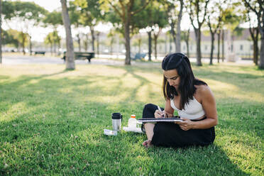 Young woman doing watercolor painting in book while sitting in park - DCRF00754