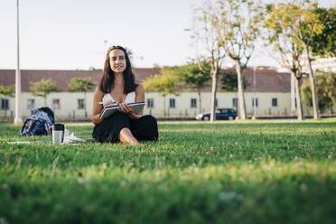 Nachdenkliche Frau mit Pinsel und Buch in einem öffentlichen Park sitzend - DCRF00756