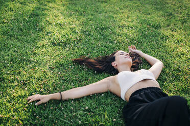 Young woman relaxing on grass at public park - DCRF00758