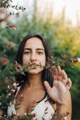 Young woman standing by flowering plant at public park - DCRF00767