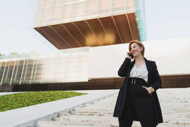 From below content female manager in elegant suit walking down the stairs in city and discussing work issues on cellphone while looking away - ADSF13199